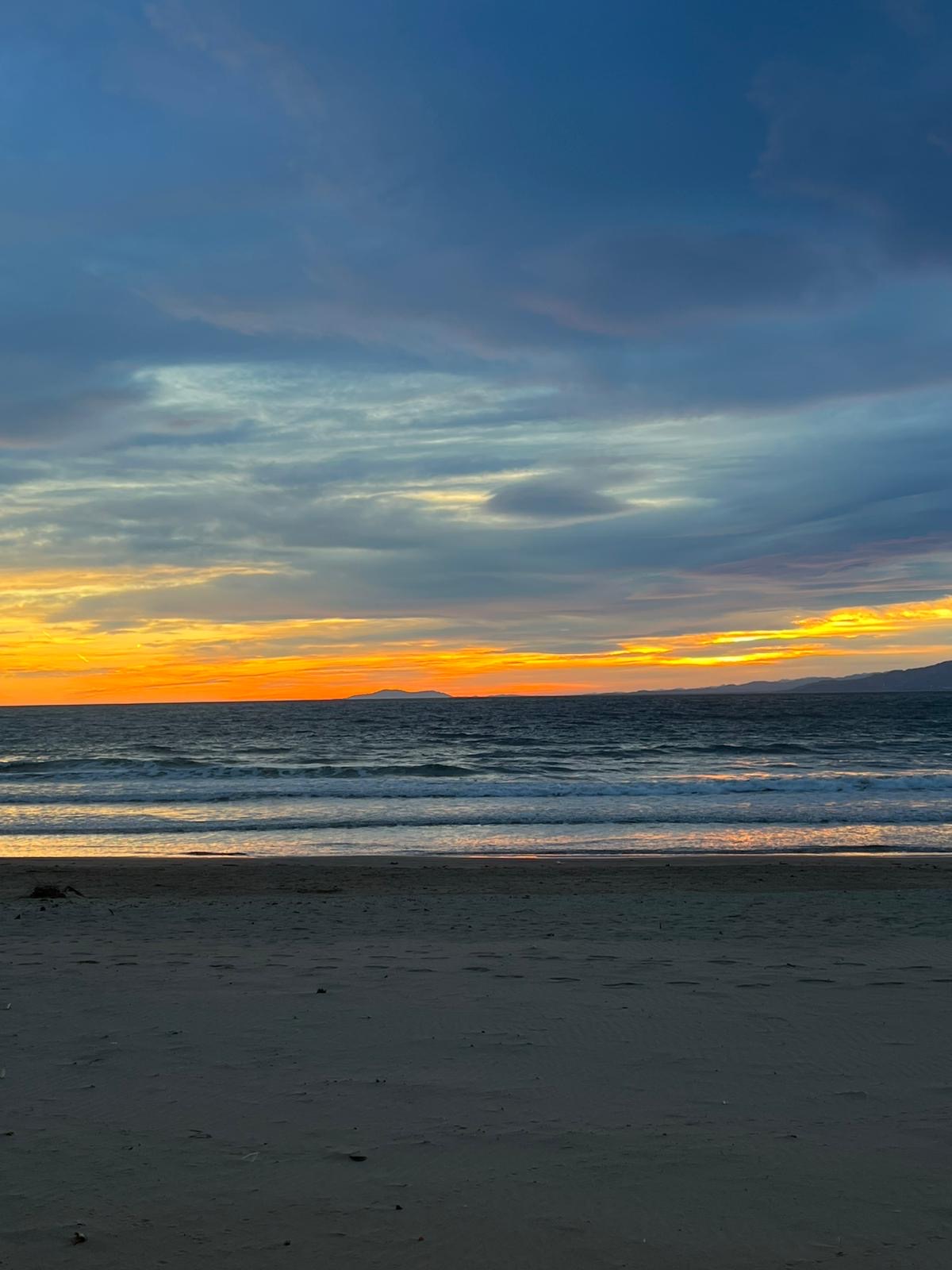 A glowing beach sunset over dark water and a quiet shoreline.